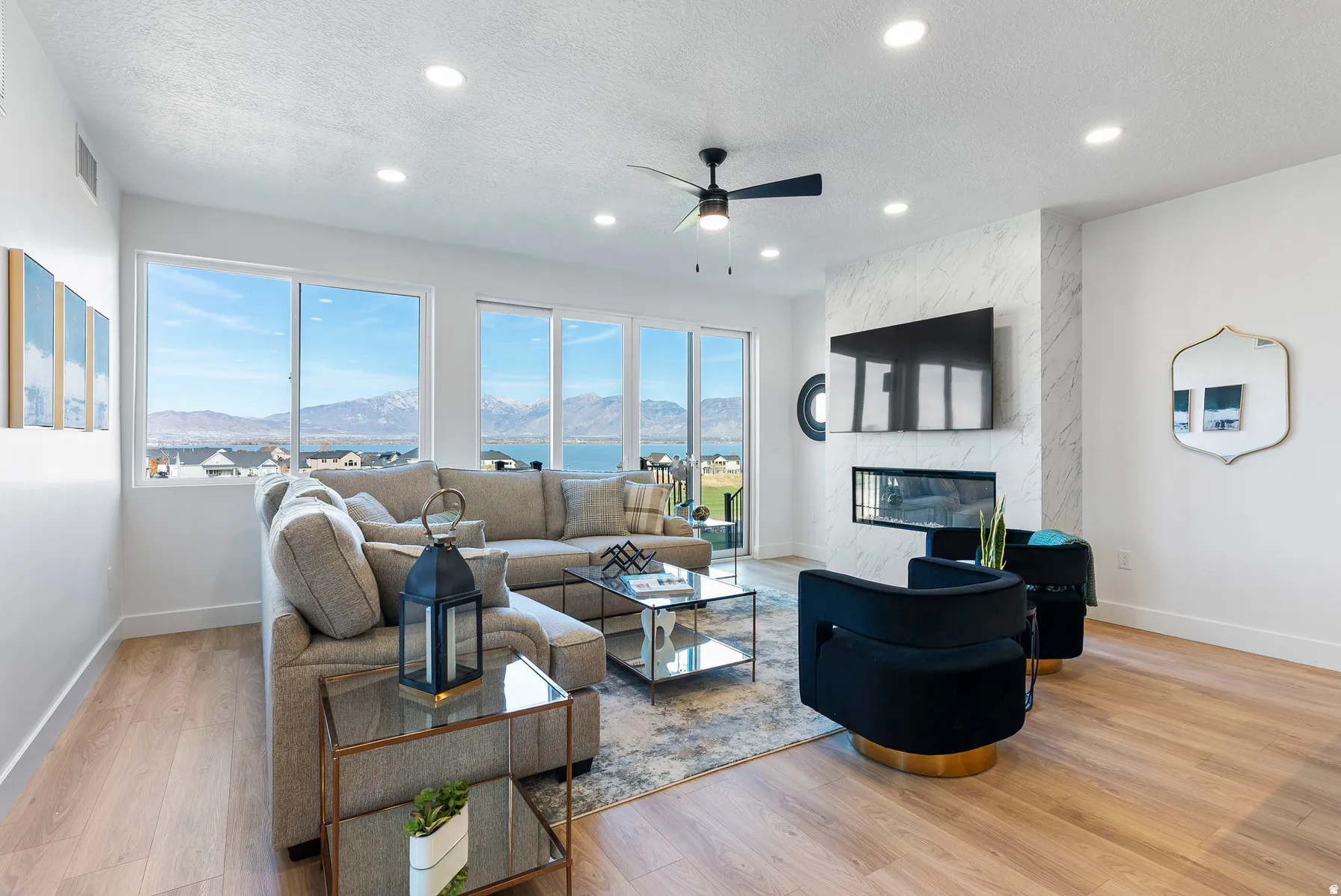 Expansive windows, wood-finish flooring, recessed lighting, ceiling fan, and a fireplace with a textured surround