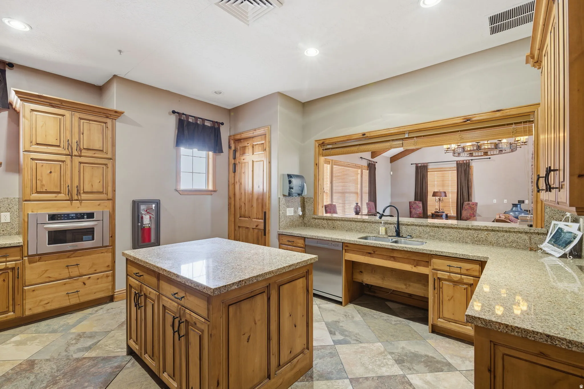 Kitchen featuring a central island, granite countertops, wood cabinetry, a built-in microwave, and tile flooring