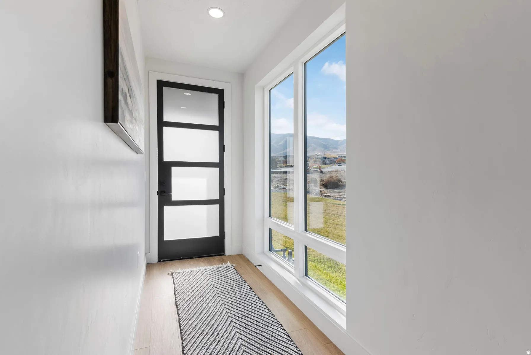 Recessed ceiling lighting, wood-finish flooring, full-light entry door with frosted panels, and large picture windows