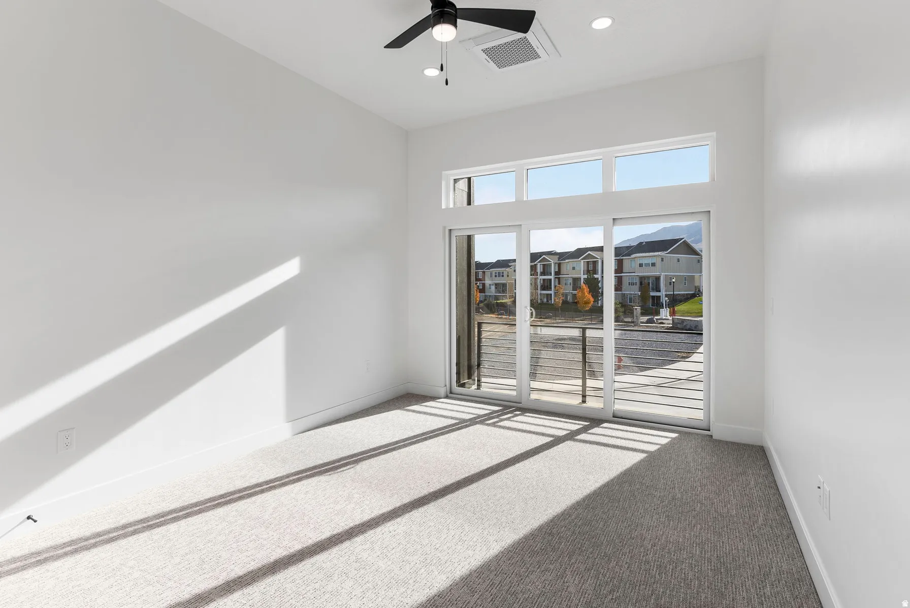 Sliding glass doors with transom windows, recessed lighting, ceiling fan, and light gray carpeting