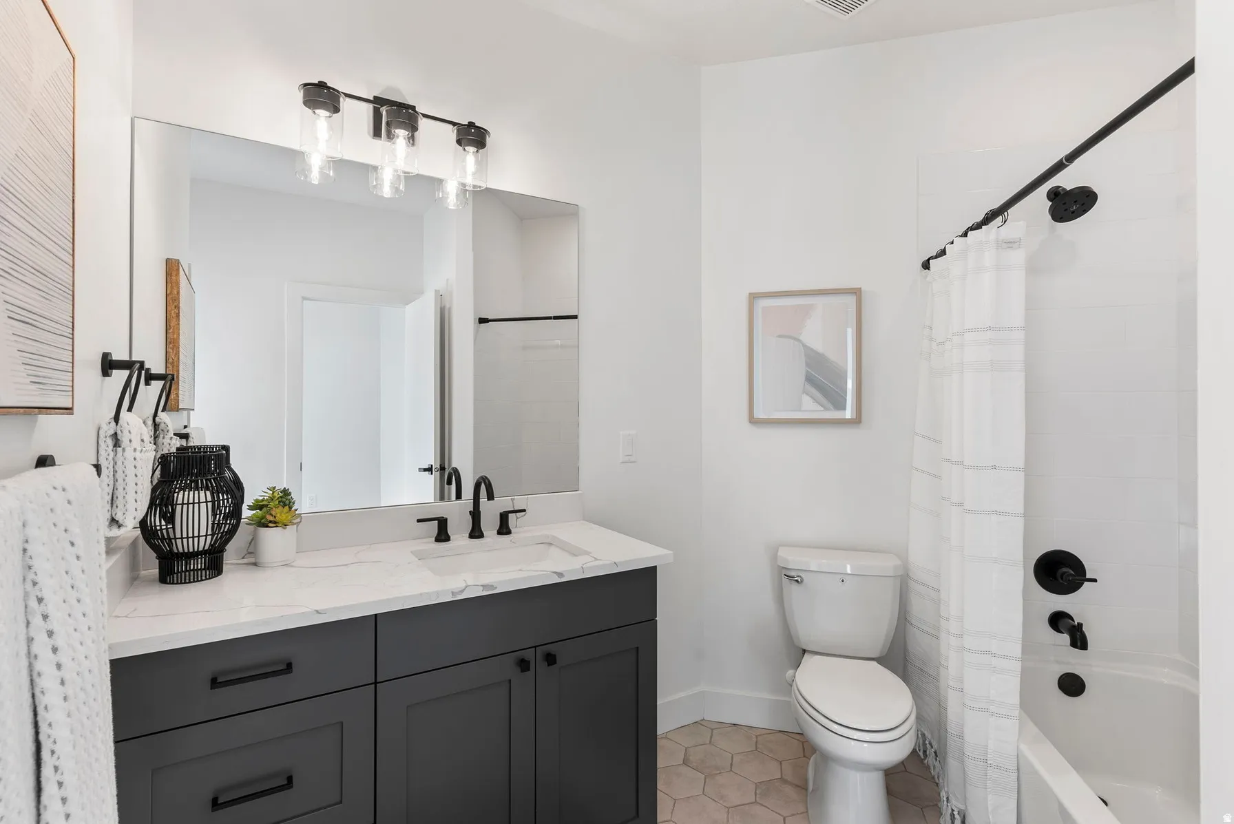 Bathroom featuring a single vanity with dark cabinetry and a light-toned countertop, a large wall-mounted mirror, a three-light vanity fixture, a toilet, and a shower-over-tub combination with black fixtures