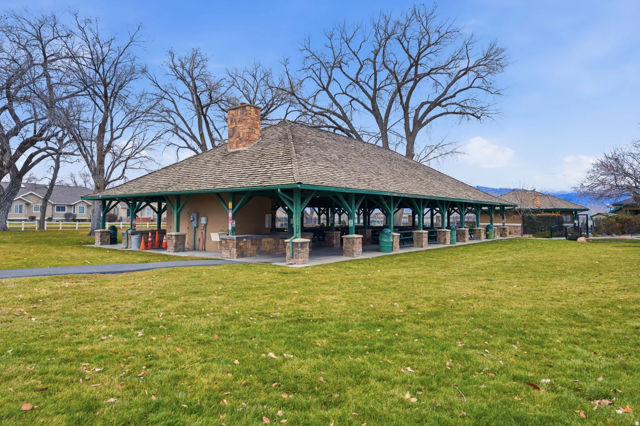 Expansive open-air pavilion featuring a shingled hip roof, exposed support beams, and a stone chimney