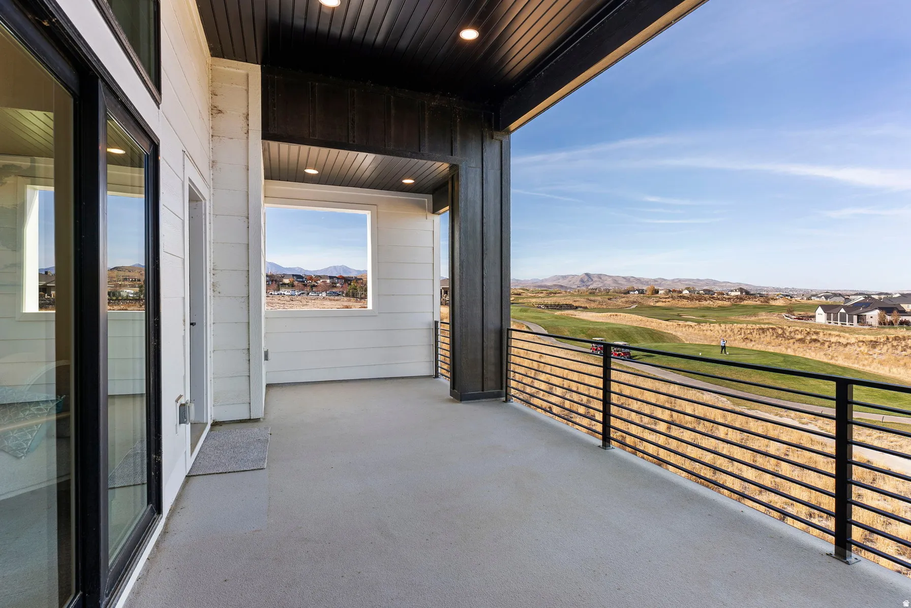 Covered outdoor balcony with a concrete surface, black metal railing, and white horizontal siding