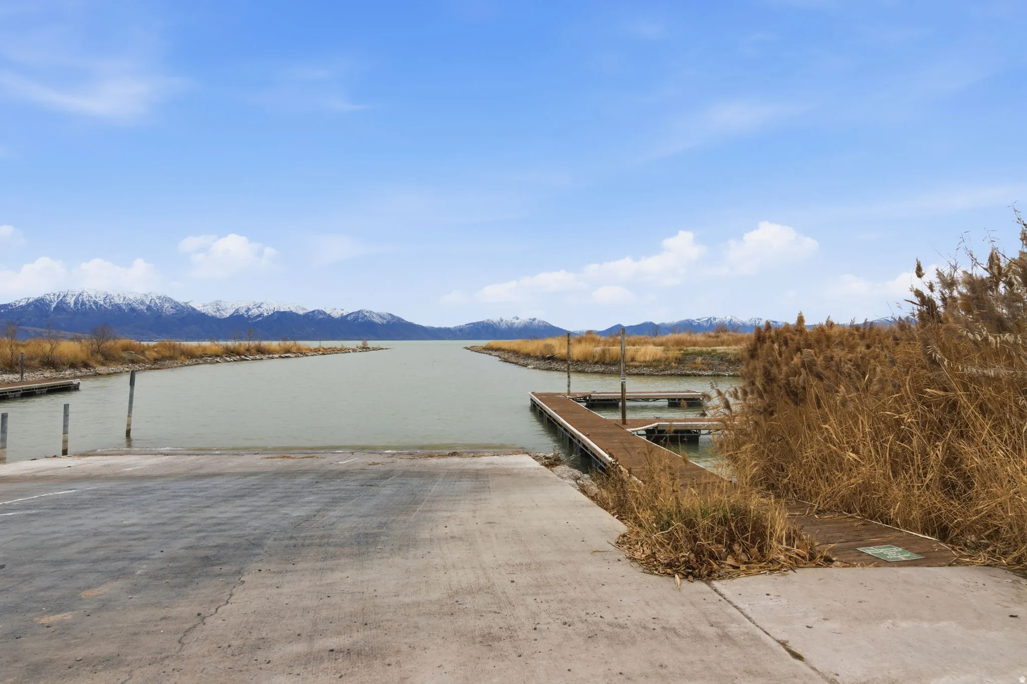 Concrete boat launch with water access, an extended dock, and snow-capped mountains in the background