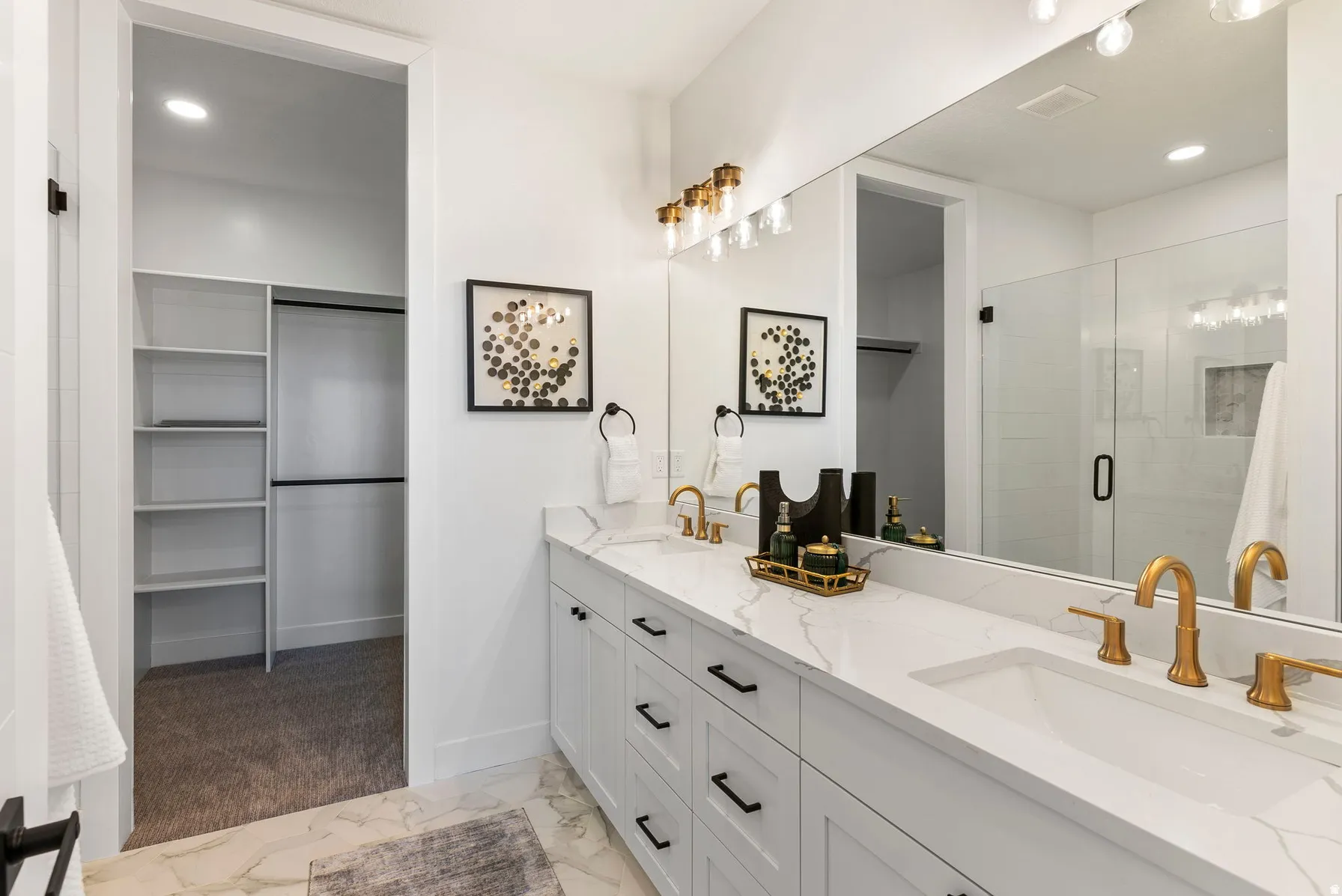 Dual vanity with white cabinetry, gold-finish fixtures, and a glass-enclosed shower