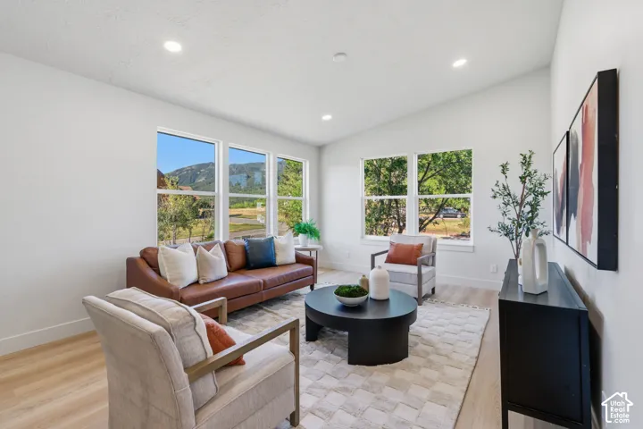 Vaulted ceiling with recessed lighting, multiple large windows, light wood-finish flooring, and white walls