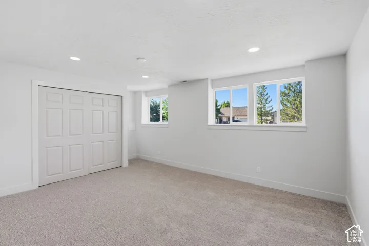 Recessed lighting, light gray carpeting, crisp white walls, white trim, and a built-in closet with paneled doors