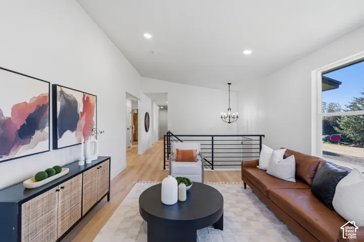 Vaulted ceiling with recessed lighting, wood-finish flooring, black metal handrail, and a chandelier over a landing