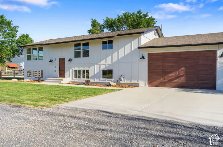 White vertical siding exterior with contrasting dark trim, integrated two-car garage with wood-finish door, concrete driveway, and established front lawn