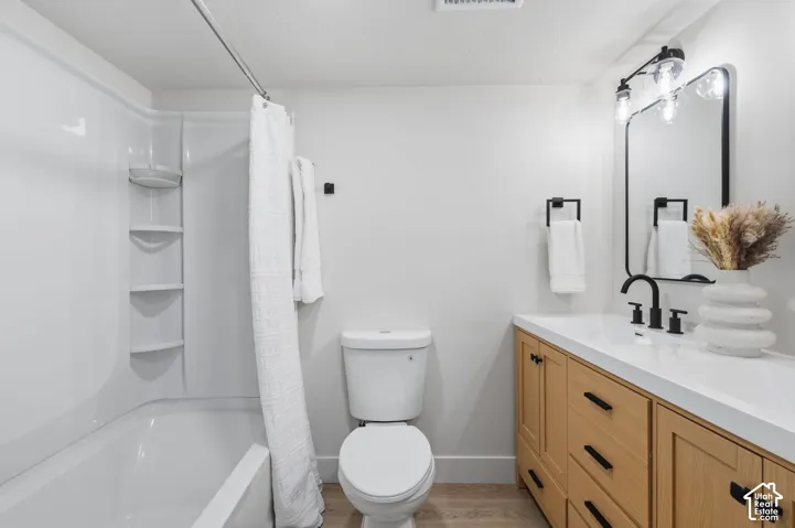 White bathtub with built-in shelving, a toilet, a wood-finish vanity with a white countertop, and a black-framed mirror with an overhead light fixture