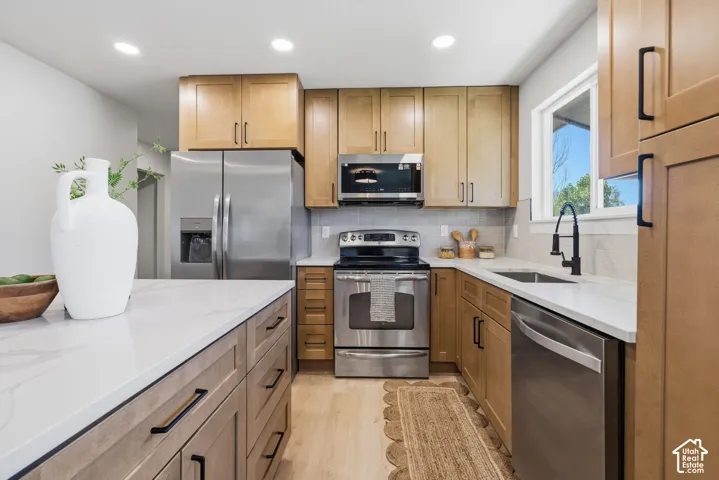 Kitchen featuring wood-finish cabinetry with matte black hardware, stainless steel appliances, white countertops, and a tile backsplash
