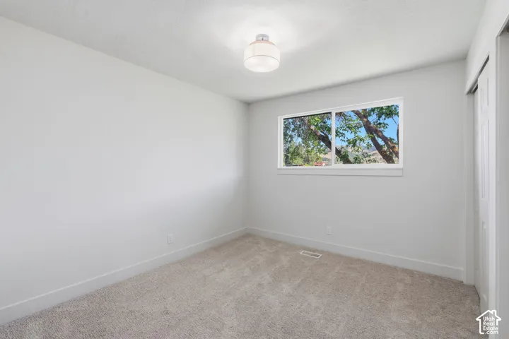 Neutral wall color, carpeted flooring, window with white trim, and a flush mount ceiling light