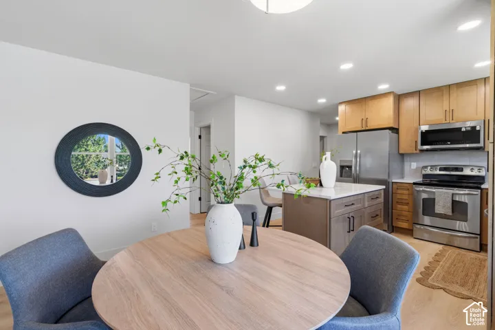 Wood-finish flooring, recessed lighting, and a kitchen featuring stainless steel appliances, light wood cabinetry, and a center island with a light-toned countertop
