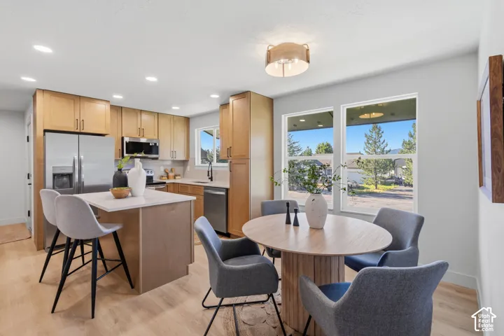Kitchen featuring light wood-finish cabinetry, stainless steel appliances, a center island with countertop seating, and light wood-finish flooring