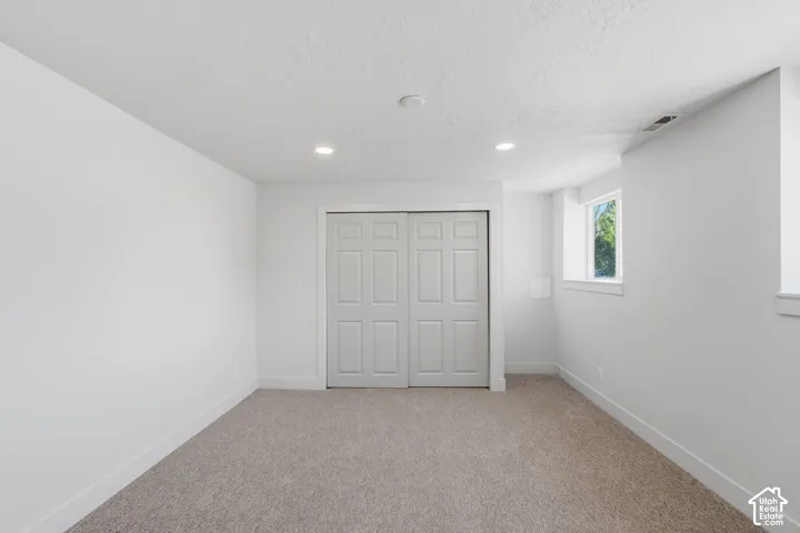 Neutral tone carpeting, recessed ceiling lighting, a window, and paneled bi-fold closet doors
