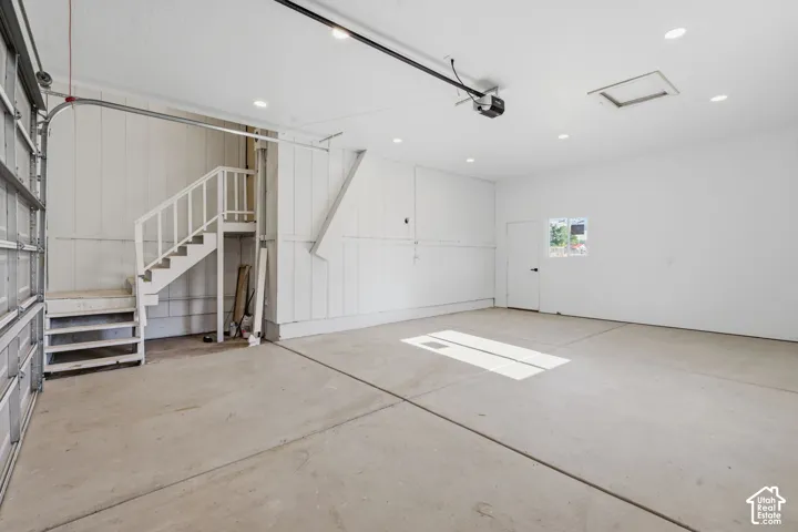 Spacious garage with concrete flooring, recessed lighting, and a built-in staircase