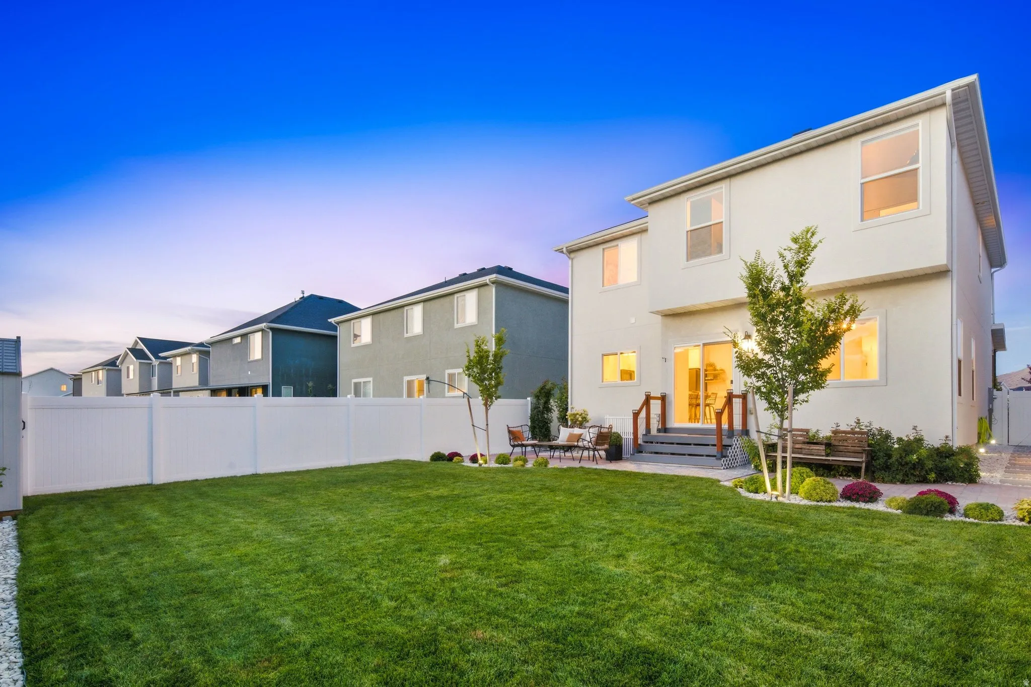 Expansive backyard with a manicured lawn, white privacy fencing, and a paved patio area