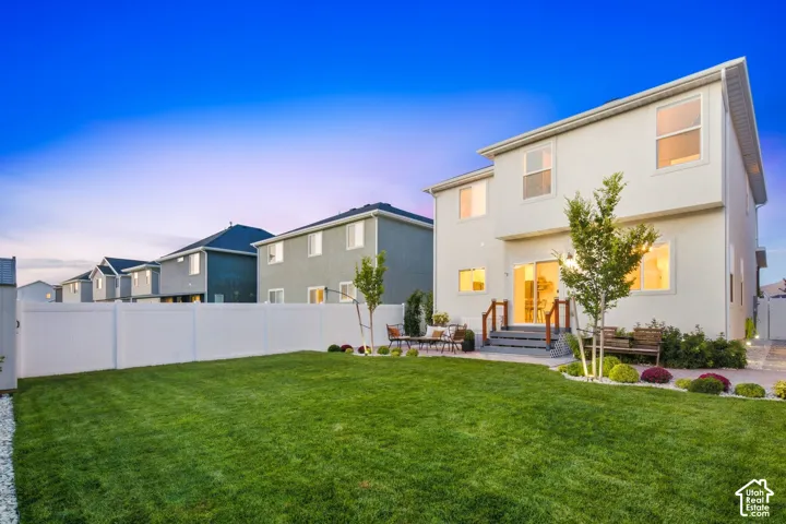 Expansive backyard with a manicured lawn, white privacy fencing, and a paved patio area