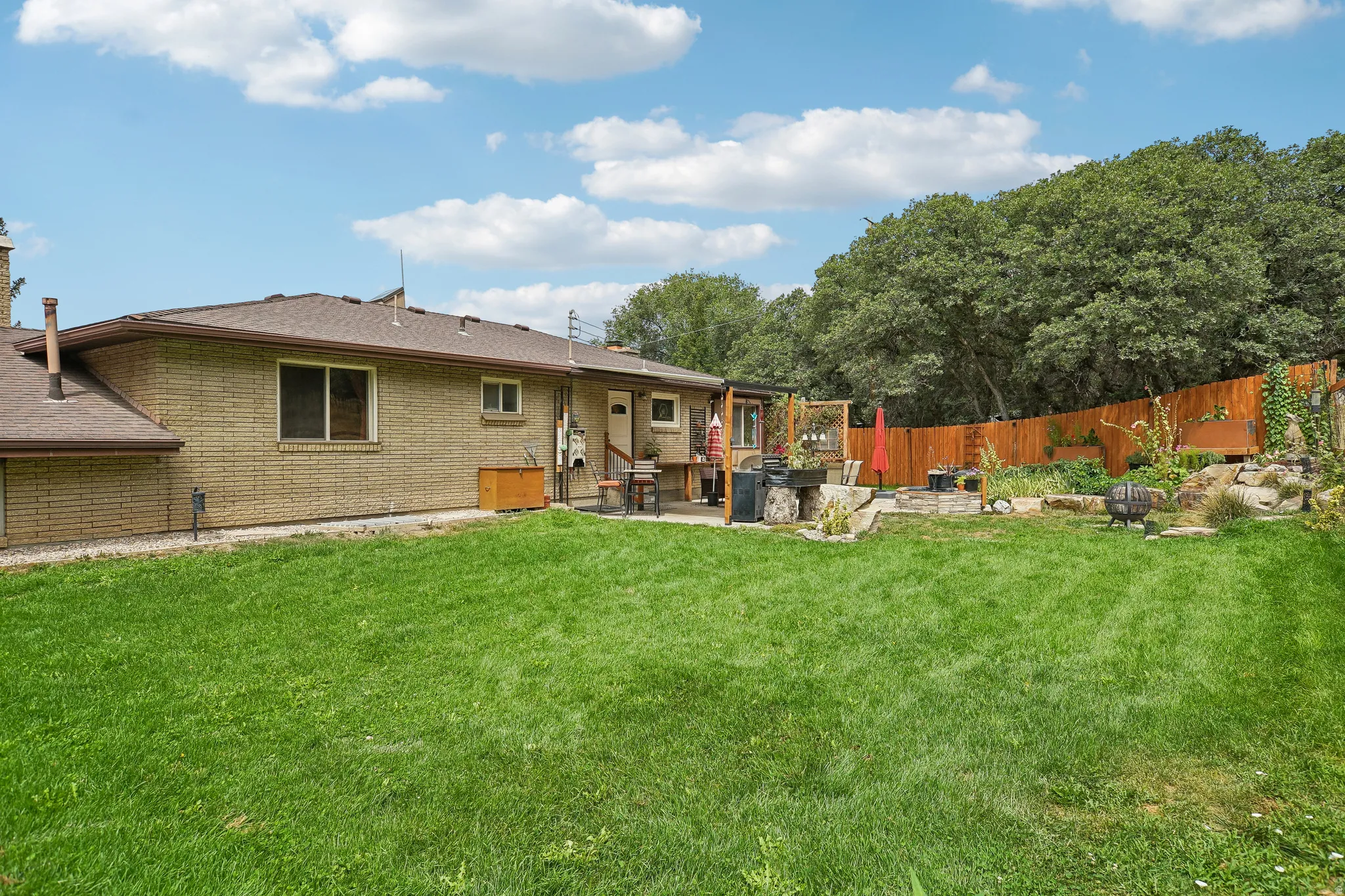 Expansive green lawn, extensive natural wood privacy fencing, mature trees, and a stone patio area