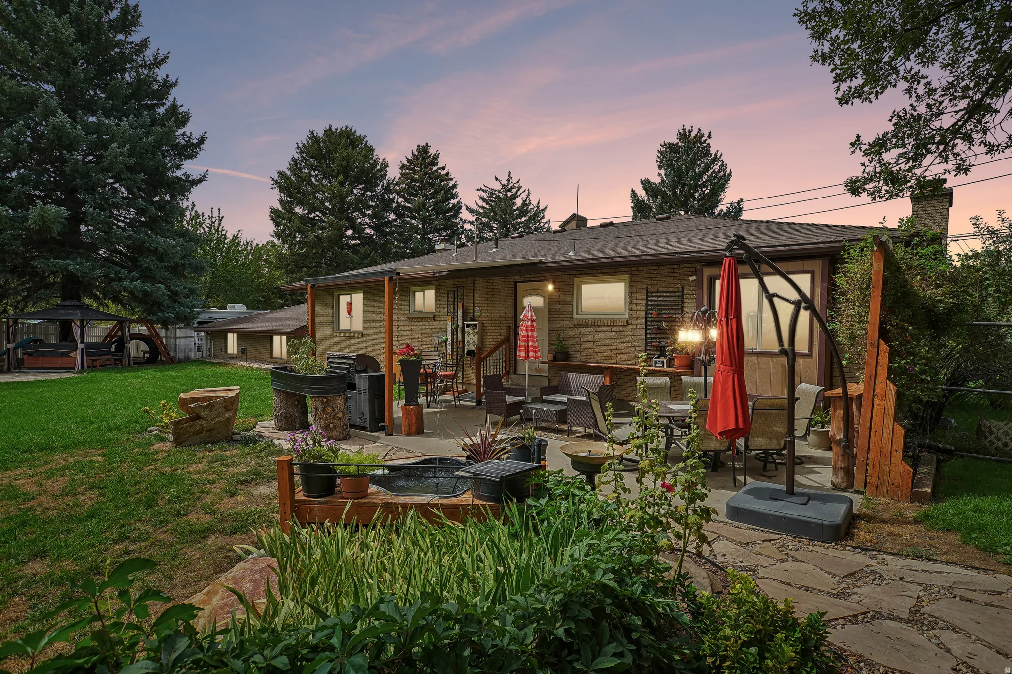 Expansive backyard with a stone patio, elevated wood deck, brick exterior, and mature trees
