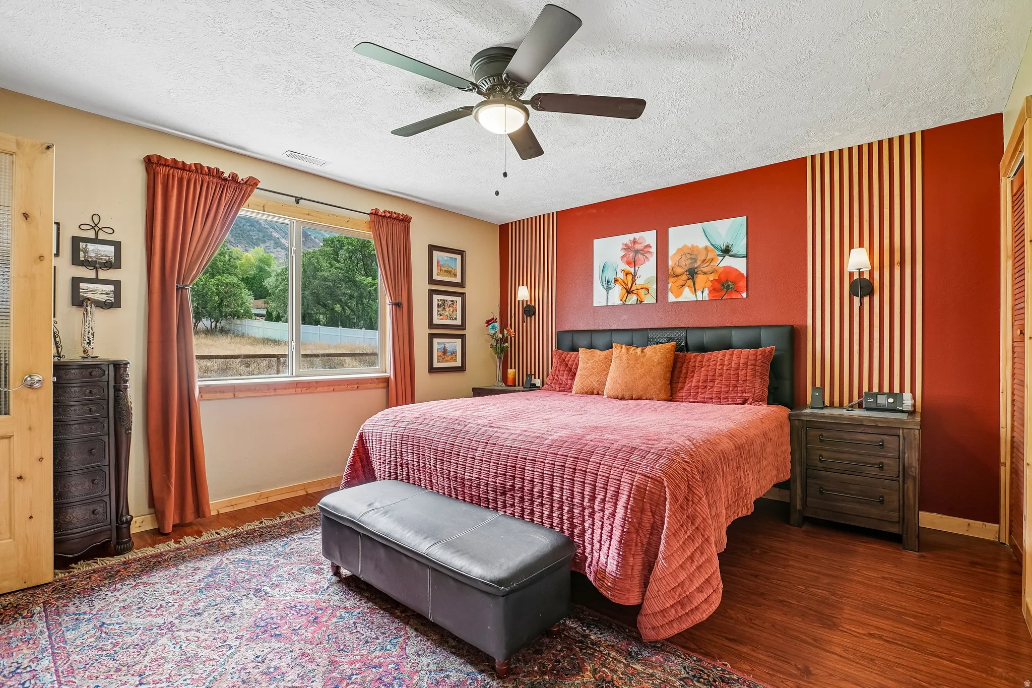 Wood-finish flooring, ceiling fan with integrated lighting, wall-mounted sconces, and a large window