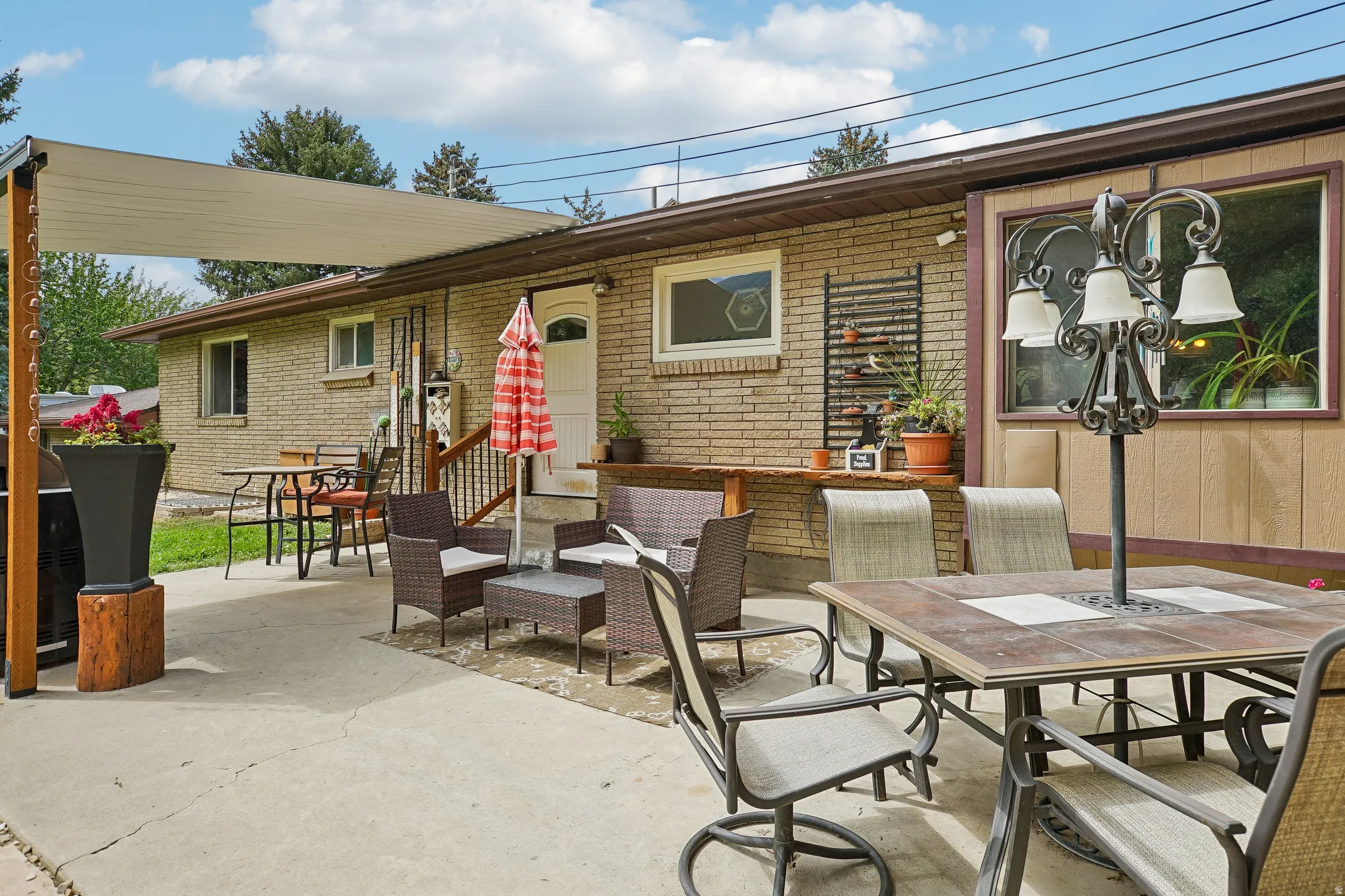 Expansive concrete patio with multiple seating and dining areas, anchored by a brick exterior with large windows and a covered entryway