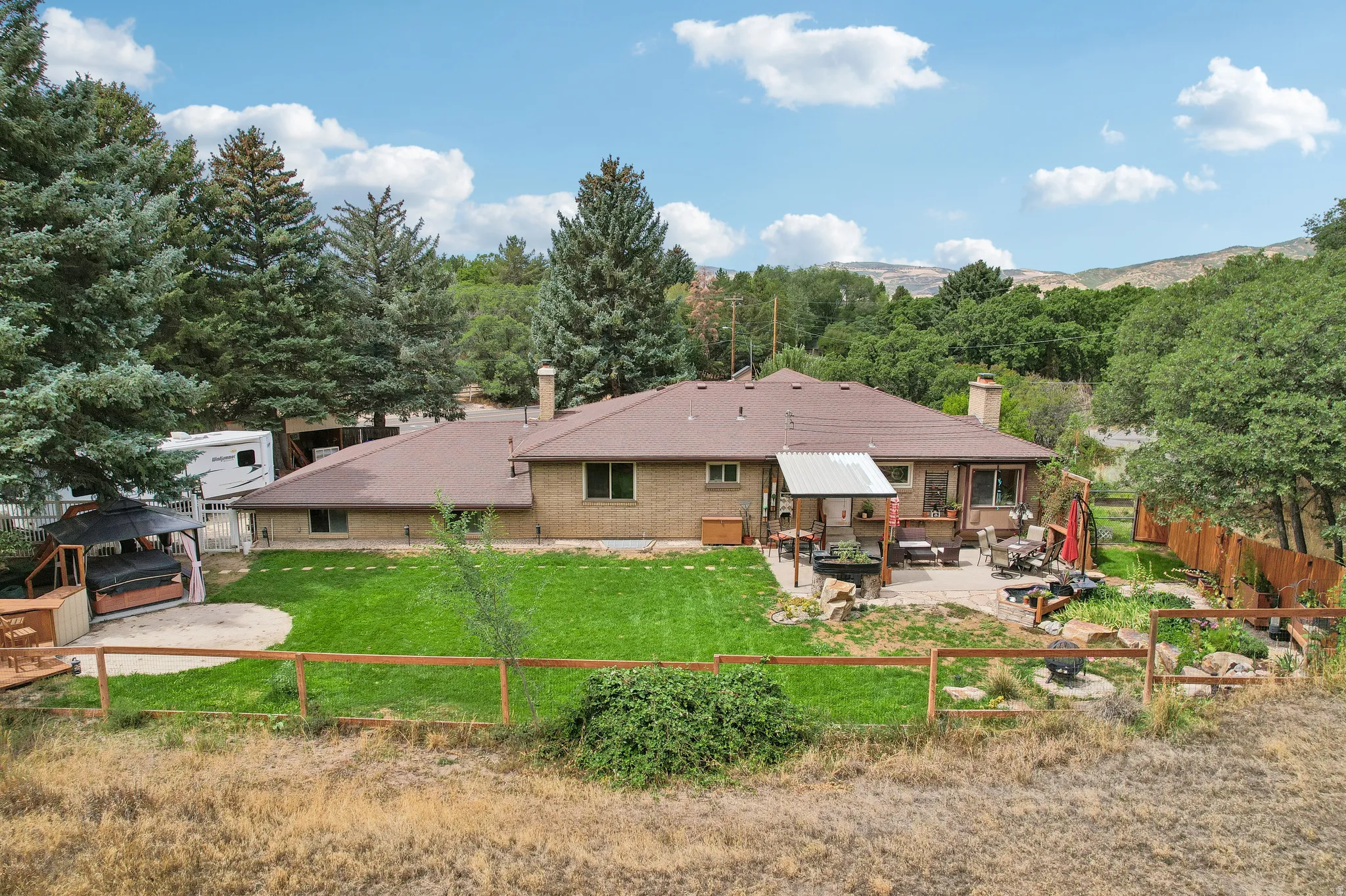 Expansive backyard featuring a manicured lawn, established trees, and a multi-level patio with a covered section