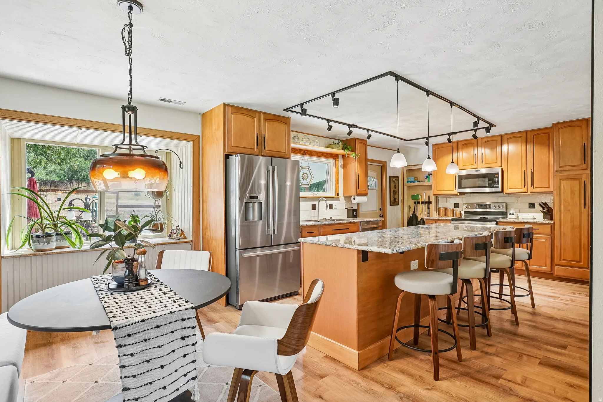 Wood-finish flooring, wood cabinetry, stainless steel appliances, central kitchen island with seating, and recessed lighting