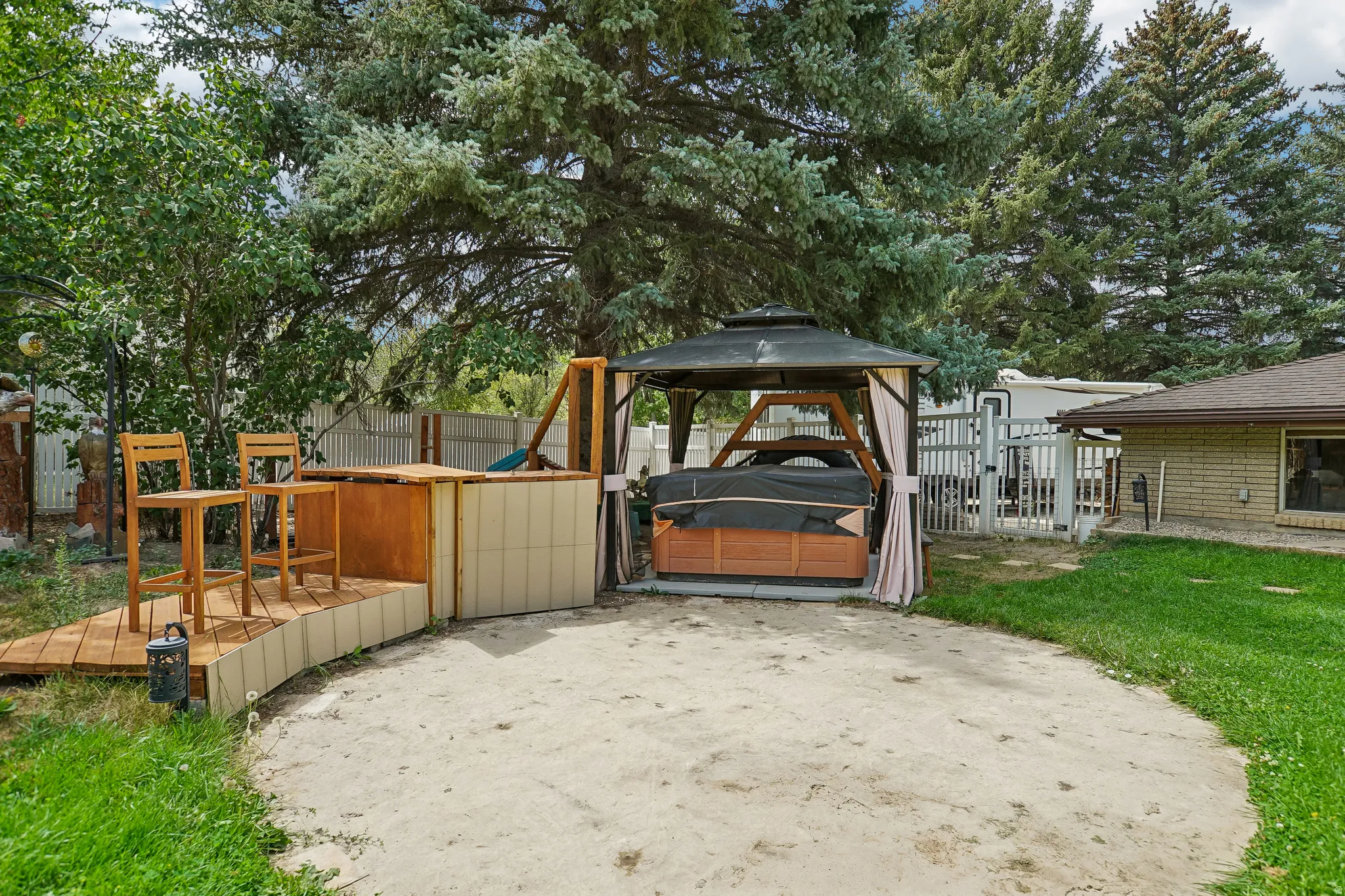 Outdoor living area featuring a covered hot tub, raised wood-finish deck with built-in bar, and mature trees