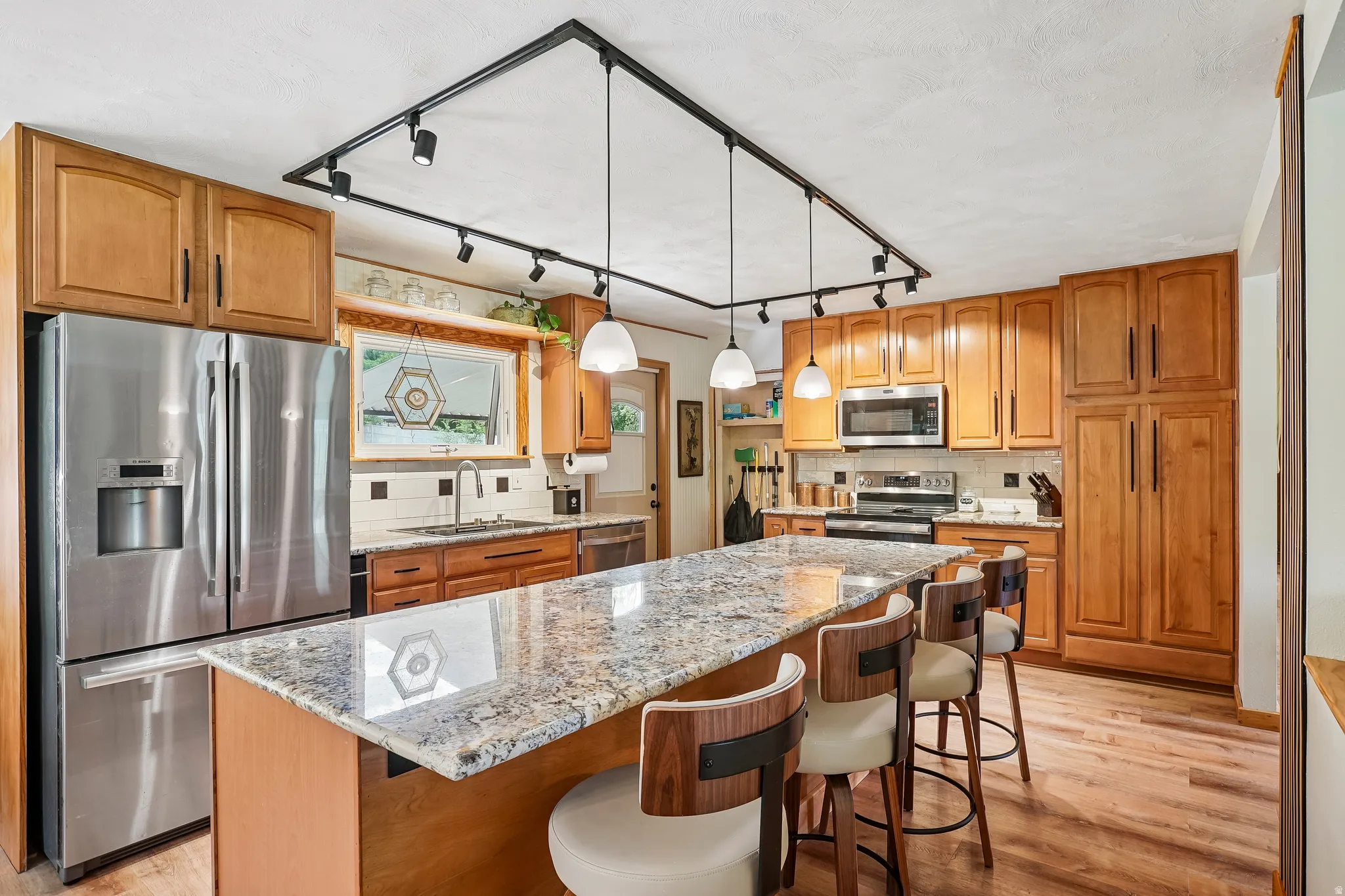 Kitchen featuring light wood cabinetry, stainless steel appliances, granite island countertop, and wood-finish flooring