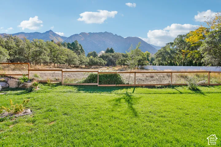 Expansive green lawn with a wood-framed wire fence, bordered by mature trees and a distant mountainous backdrop