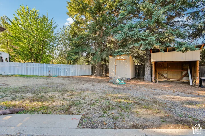 Expansive lot featuring a white privacy fence, mature trees, a detached storage shed, and an open-sided storage structure