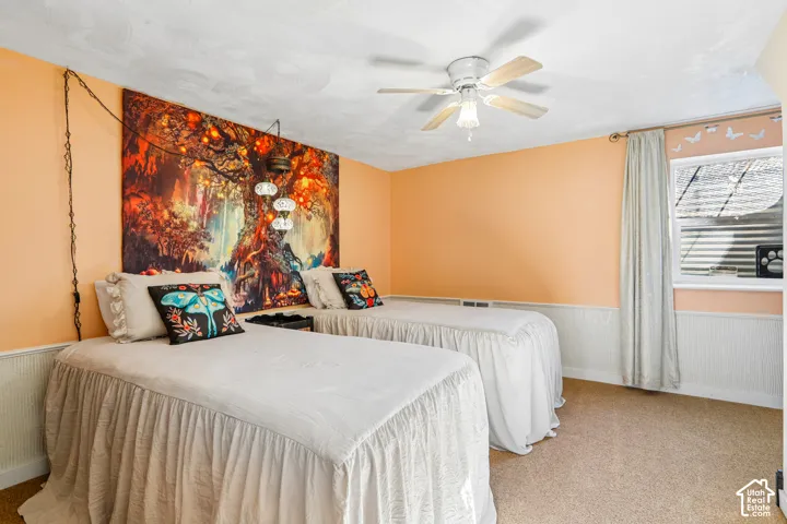 Carpeted flooring, window with blinds, ceiling fan, and white wainscoting