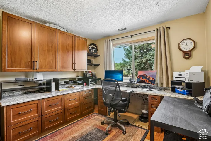 Home office featuring warm wood cabinetry with ample storage, granite countertops, a large work surface with black laminate finish, and abundant natural light from a sliding glass door overlooking mature landscaping