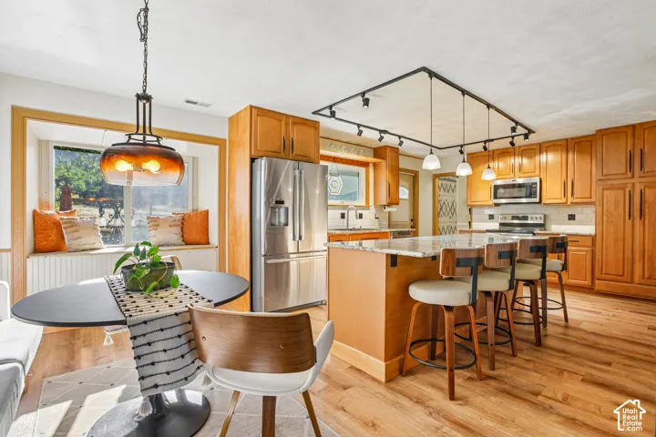 Wood-finish flooring throughout, featuring a kitchen island with seating, pendant lighting, and stainless steel appliances