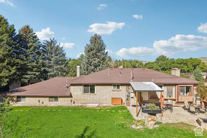 Expansive lawn area with mature trees, a covered patio, and a stone-paved outdoor entertaining space