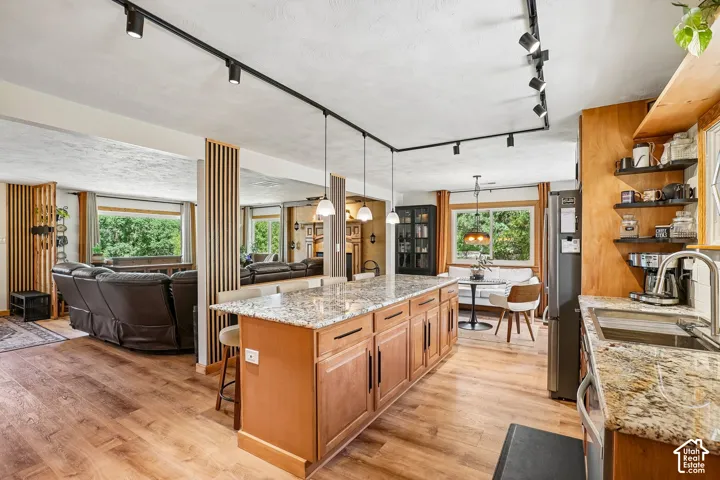 Open-concept kitchen and living area featuring a large wood-finish island with stone countertops, stainless steel appliances, hardwood flooring throughout, abundant natural light from multiple windows, and track lighting
