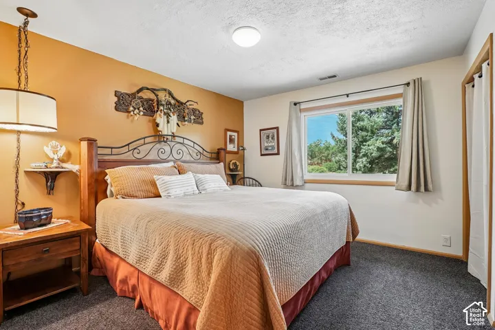 Recessed ceiling lighting, carpet flooring, a window with exterior scenery, and a wooden bed frame with an ornate headboard