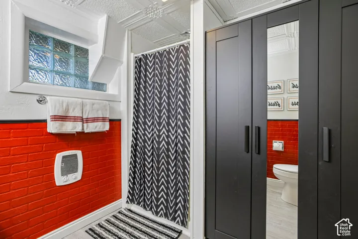 Shower enclosure with glass block window, red brick-patterned wall, and textured ceiling