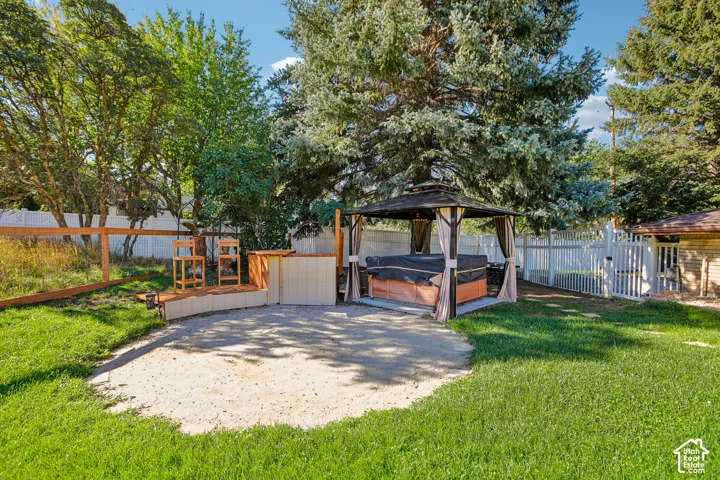 Expansive backyard featuring a hot tub within a gazebo, wood deck, and perimeter fencing