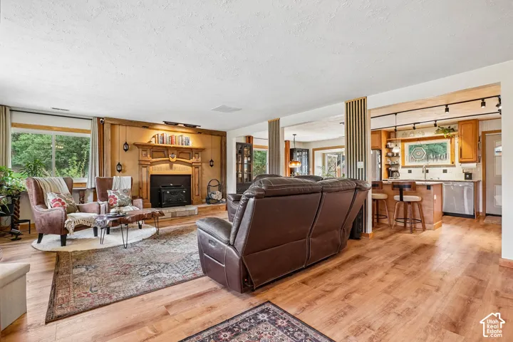 Wood-finish flooring throughout, featuring a fireplace with ornate wood mantel, large window, and an open kitchen with breakfast bar seating and built-in cabinetry