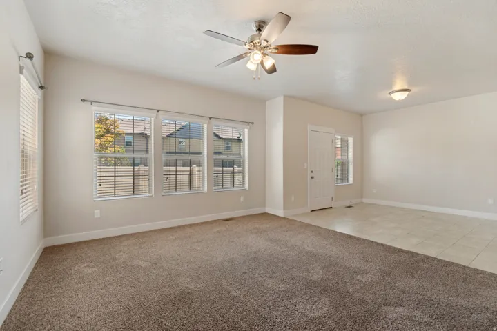 Vaulted ceiling, ceiling fan with light fixture, carpeted flooring, tiled flooring, multiple windows with blinds