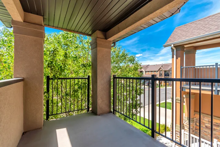 Covered balcony with stucco columns, black metal railings, and a soffit ceiling