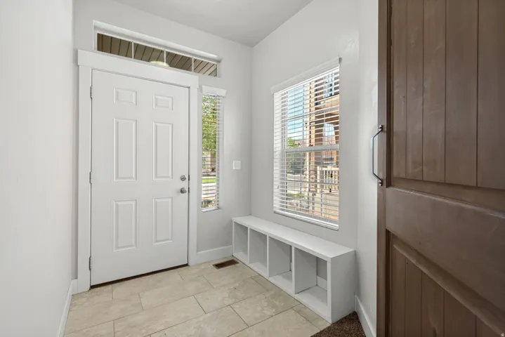 Tiled flooring entry with a white paneled door, transom window, and an integrated storage bench