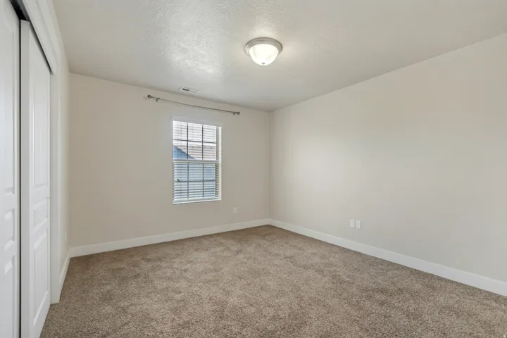 Carpeted room featuring a window with blinds, a ceiling-mounted light fixture, and sliding closet doors