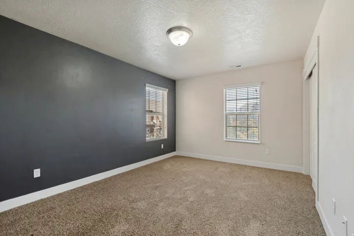 Neutral wall colors with a contrasting accent wall, two windows with blinds, wall-to-wall carpeting, and a ceiling-mounted light fixture