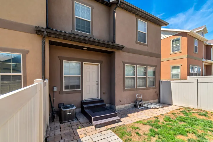 Stucco exterior with multiple windows, paneled door, three-step entry, and paver patio