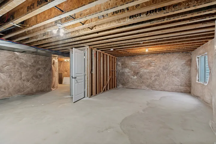 Unfinished basement with exposed ceiling joists, concrete flooring, framed interior walls, and an egress window opening