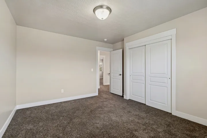 Neutral wall paint, textured carpet flooring, white trim, sliding panel closet doors, and an overhead flush-mount light fixture