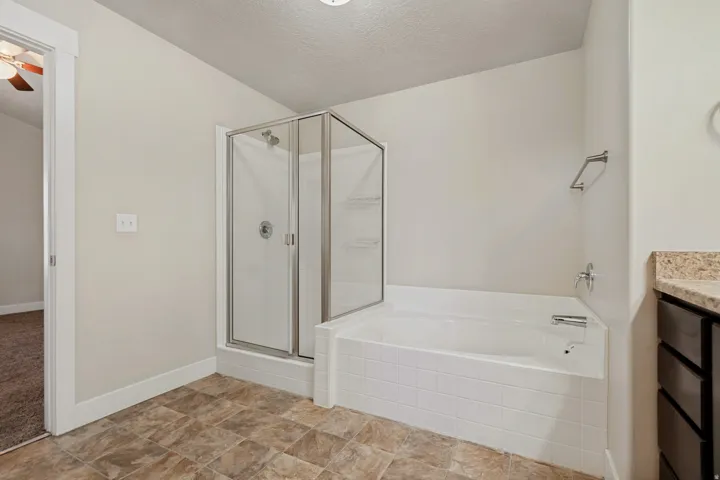 Walk-in shower with glass enclosure, separate soaking tub, and vanity with stone-look countertop
